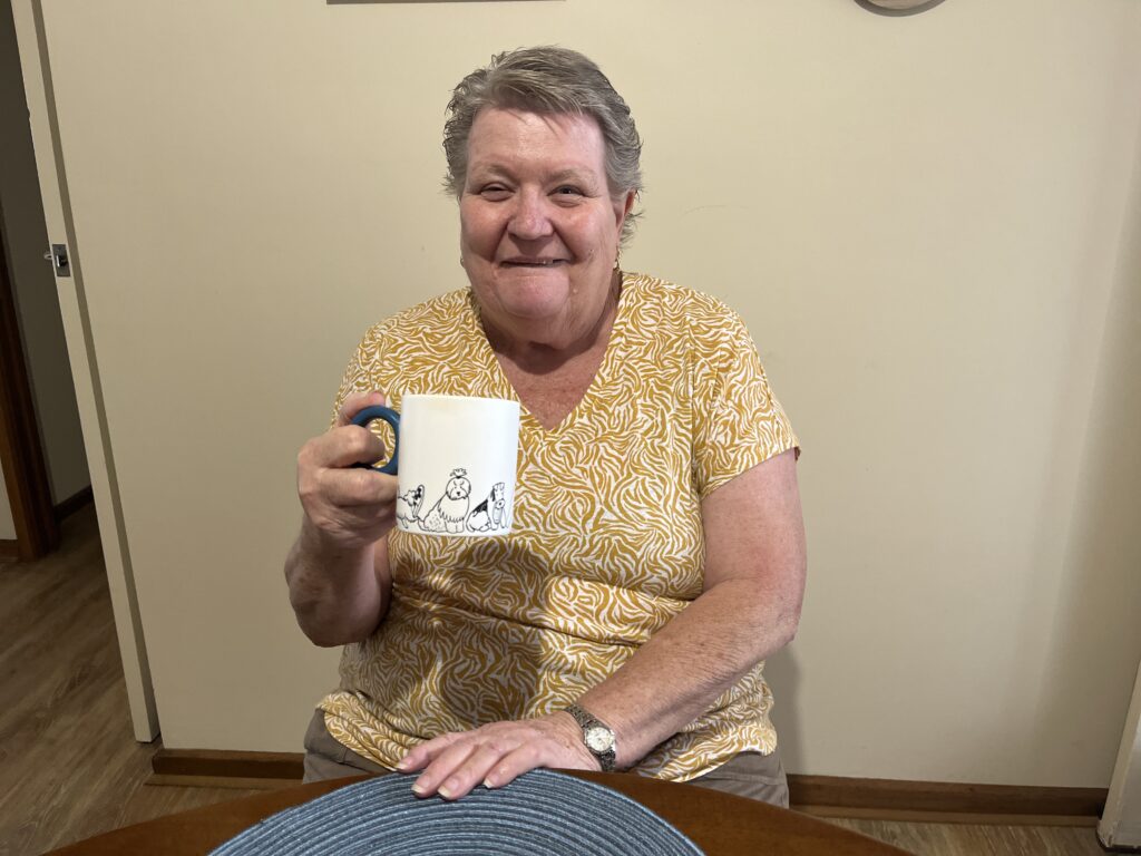 BHA tenant Deb sits smiling with her cup of coffee in hand. 